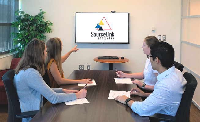 Four professionals in a conference room, one pointing to screen